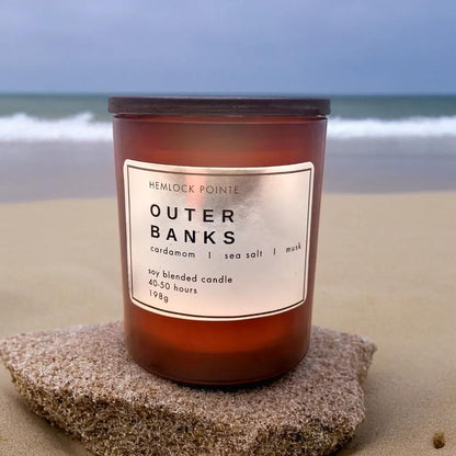 a hemlock pointe outer banks candle sits on a rock on the beach