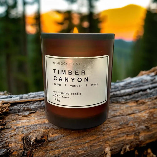 a candle called timber canyon sits on a log