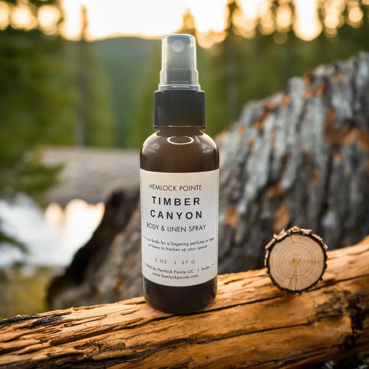 a bottle of hemlock pointe timber canyon body & linen spray sitting on log in front of wooded background